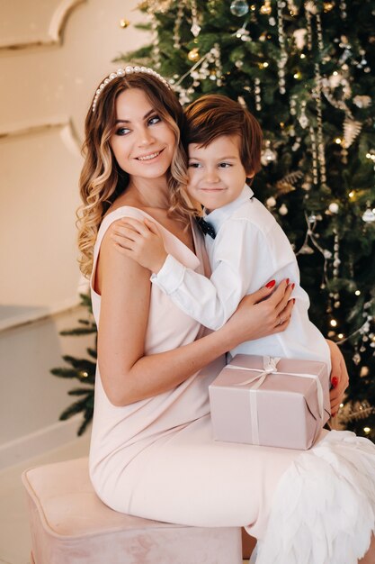 Mamá le da a su hijo un regalo de Navidad cerca del árbol de Navidad. Familia feliz.