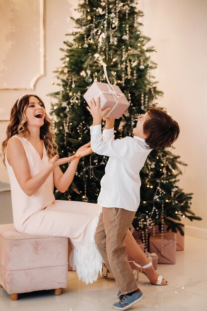 Mamá le da a su hijo un regalo de Navidad cerca del árbol de Navidad. Familia feliz.