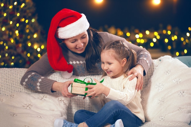 Mamá dando un regalo a su pequeña niña en el sofá