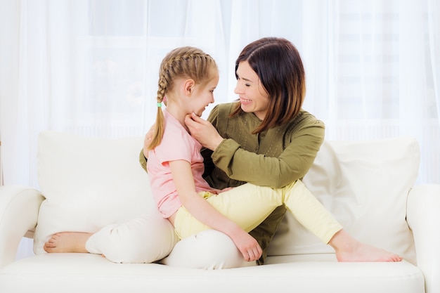 Mamá divertida y niña adolescente relajándose en el sofá blanco