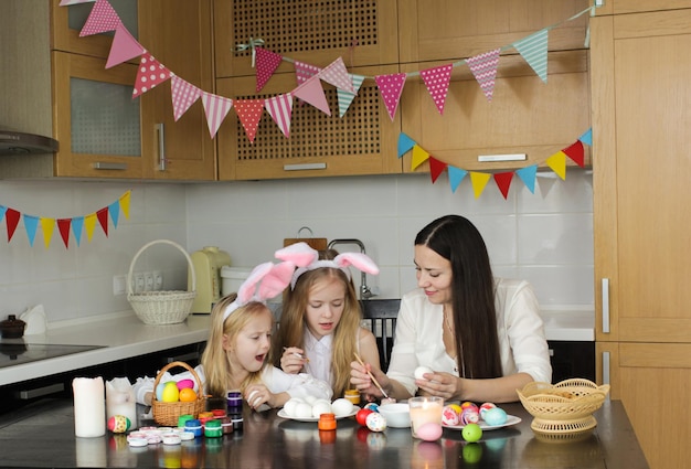 Mamá y dos hijas pequeñas dibujan huevos de Pascua. Una familia feliz se prepara para la Pascua.