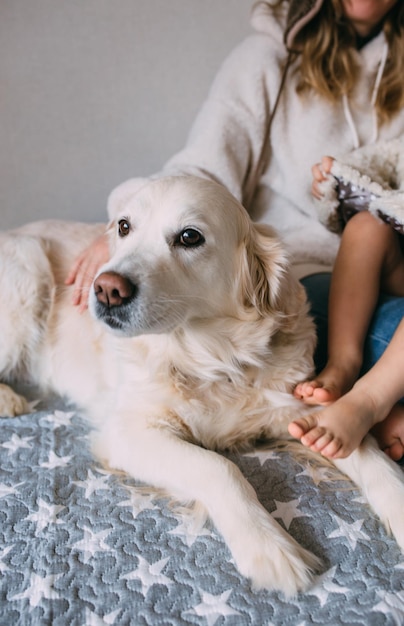 Mamá e hija se abrazan cómodamente en casa con su mascota labrador retriever