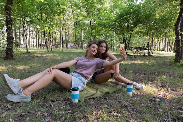 Mamá e hija adolescente toman un selfie mientras caminan en un parque de verano. Usando un teléfono inteligente