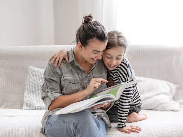 Mamá e hija alegres están descansando en casa, leyendo un libro juntas. concepto de una familia feliz y relaciones amistosas.