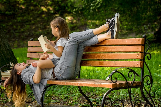 Mamá e hija en un banco leen un libro en el parque, el concepto de relaciones familiares y valores familiares