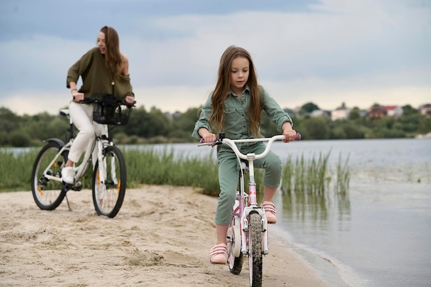 Mamá e hija en bicicleta cerca del río Concepto de vacaciones de verano para niños