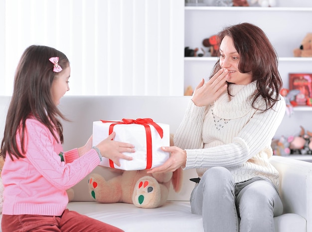 Mamá e hija con caja de regalo sentada en el sofá el concepto de sorpresa