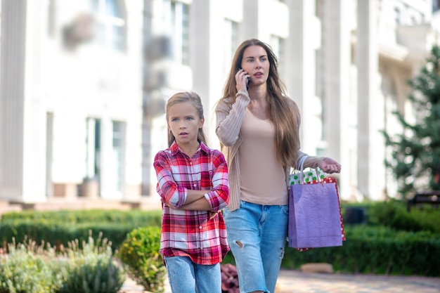 Foto mamá e hija caminando por la calle con bolsas de la compra.