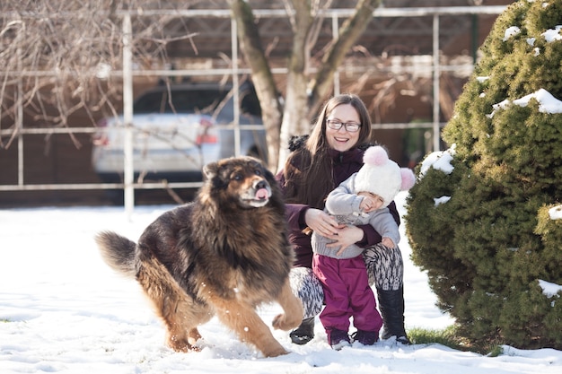 Mamá e hija caminando en un día de invierno y juegan con su perro