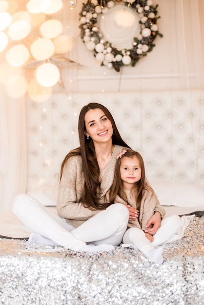 Mamá e hija en casa en el fondo de un árbol de Navidad. Familia en la cama