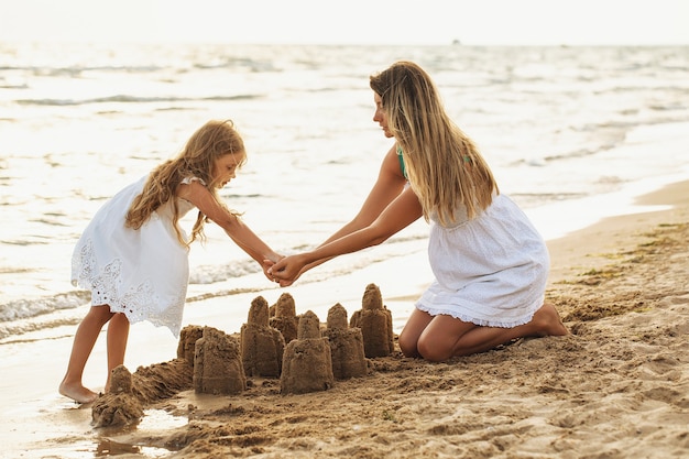 Mamá e hija construyen castillos de arena en la playa en un día soleado de verano