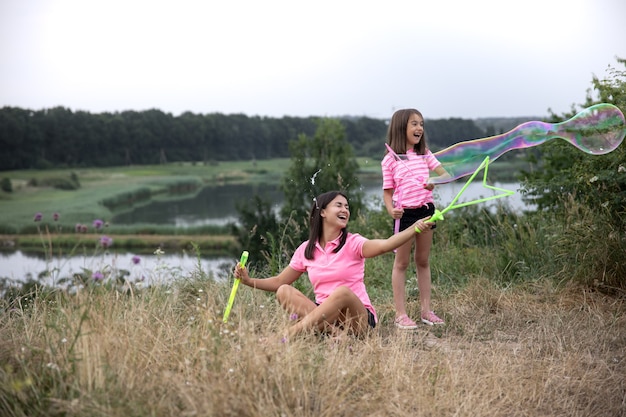 Mamá e hija se divierten juntas, hacen grandes pompas de jabón, recreación al aire libre.