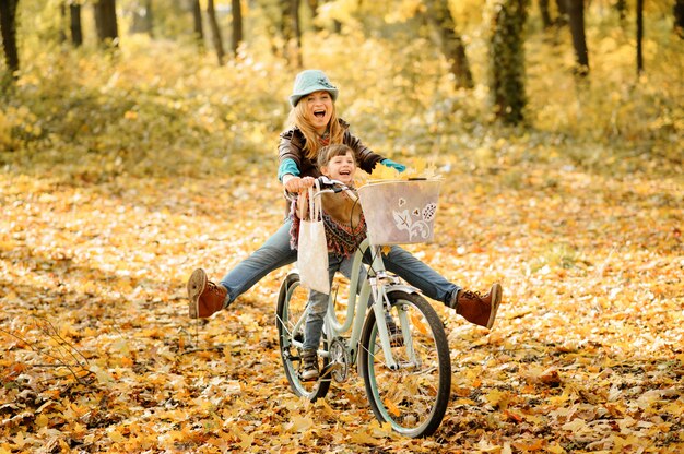 Mamá e hija se divierten en la misma bicicleta. Sesión de fotos de otoño.