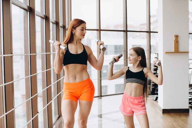 Mamá e hija están haciendo ejercicios. Familia en un gimnasio. Niña con madre fuerte están entrenando con pesas