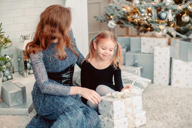 Mamá e hija están mirando los regalos de Año Nuevo mientras están sentados en el fondo de un árbol de Navidad decorado