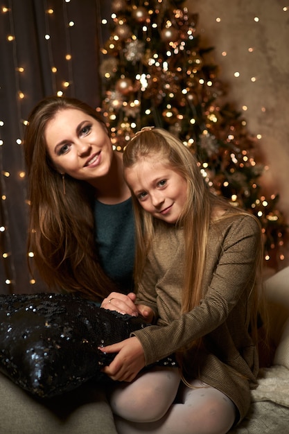 Mamá e hija están sentadas cerca del árbol de Navidad