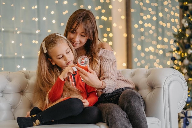 Mamá e hija están sentadas juntas en la casa, esperando la magia navideña. En vísperas de Navidad con mi madre.