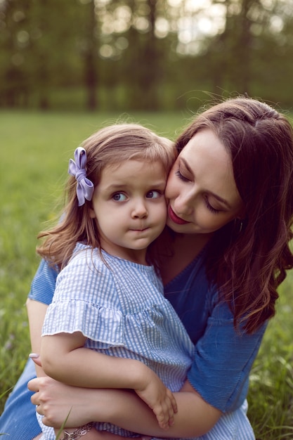 Mamá e hija están sentadas en un prado verde con vestidos azules