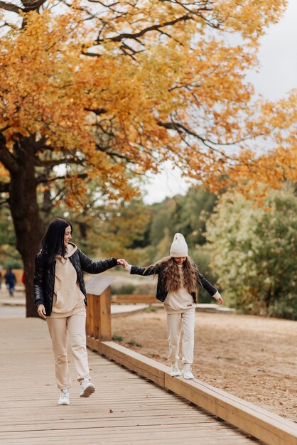 Mamá e hija con estilo en chaquetas de cuero caminan juntas en el parque de otoño