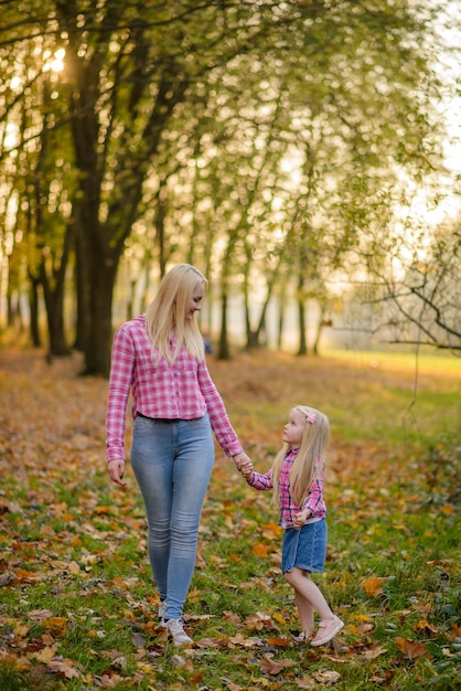 Mamá e hija en jeans y camisas rosas caminan en el parque de otoño.