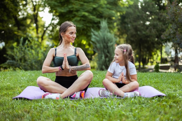 Mamá e hija meditan practicando yoga juntos en la alfombra en el parque Maternidad Pasando tiempo Mamá Entrenador concepto de familia saludable
