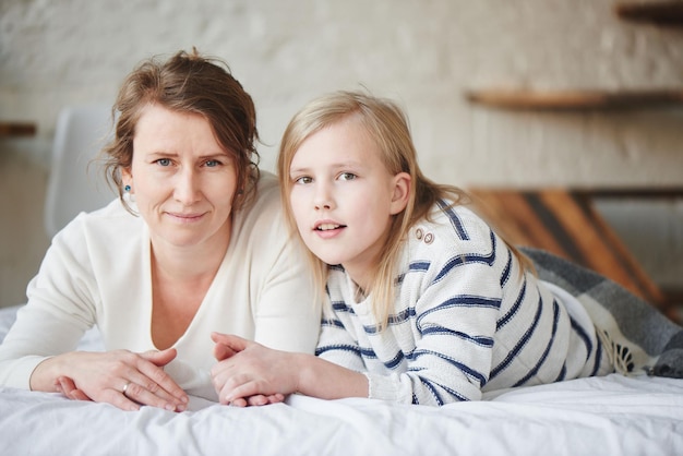 Mamá e hija mienten en una cama blanca en casa