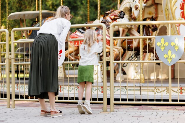 Mamá e hija miran el carrusel en el parque en verano