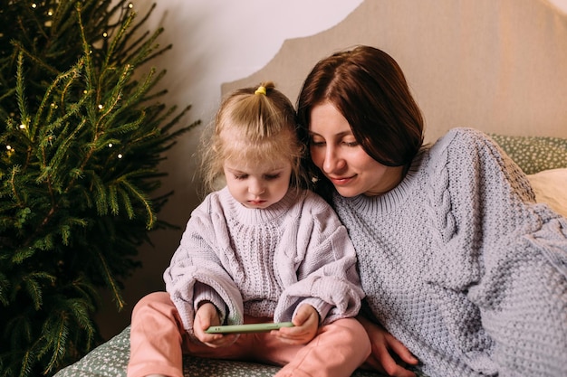 Mamá e hija miran juntos el teléfono inteligente en Navidad