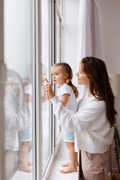 Mamá e hija miran por la ventana de la casa.