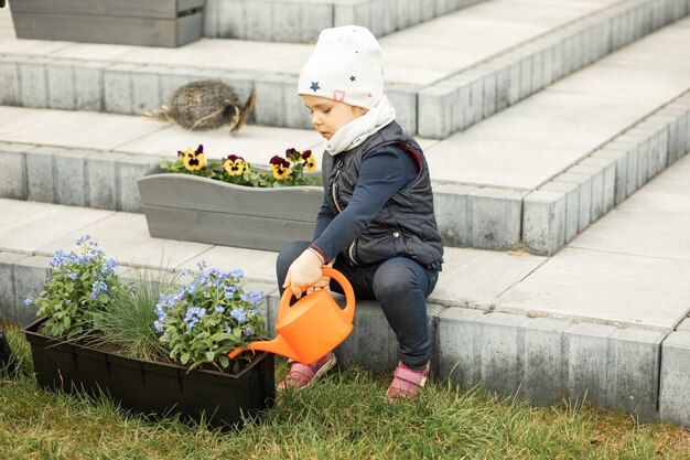 Mamá e hija pasan tiempo juntas en el frente o en el patio trasero de la casa, plantando flores, niña regando nomeolvides con regadera, atrayendo a los niños a la tarea