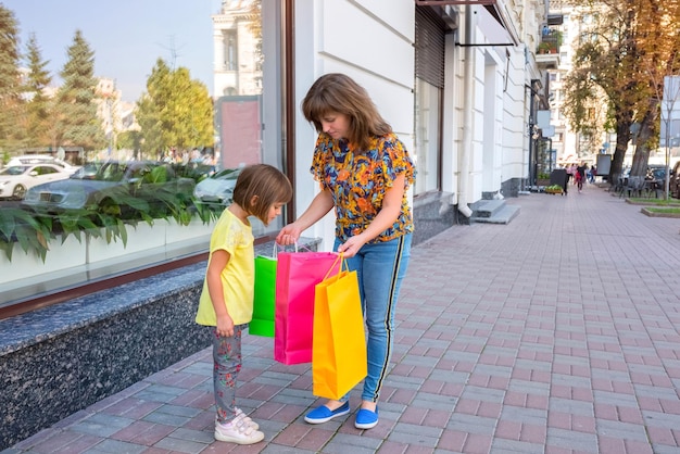 Mamá e hija pequeña sosteniendo bolsas de compras niña mirando compras en paquetes