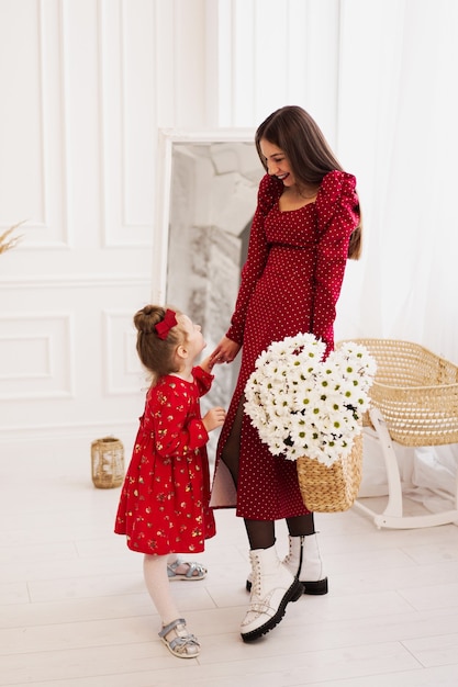 Mamá e hija pequeña en vestidos rojos en una habitación luminosa