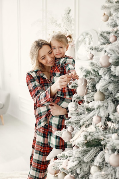 Mamá e hija en pijama a cuadros abrazándose cerca del árbol de Navidad