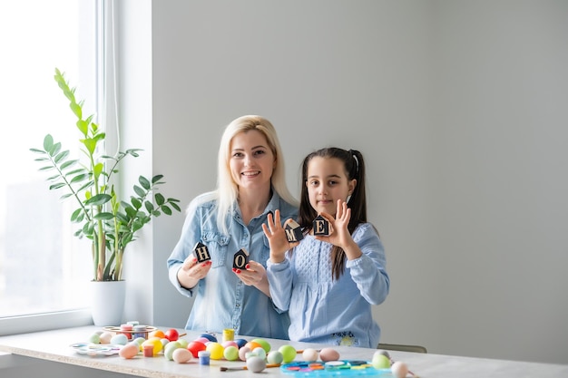 Mamá e hija pintan huevos con colores. Divertirse. La familia feliz se está preparando para la Pascua, mantén la inscripción en casa.