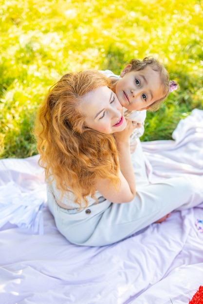 Mamá e hija riendo y abrazándose sentados en una manta en el parque el concepto de una familia feliz ...