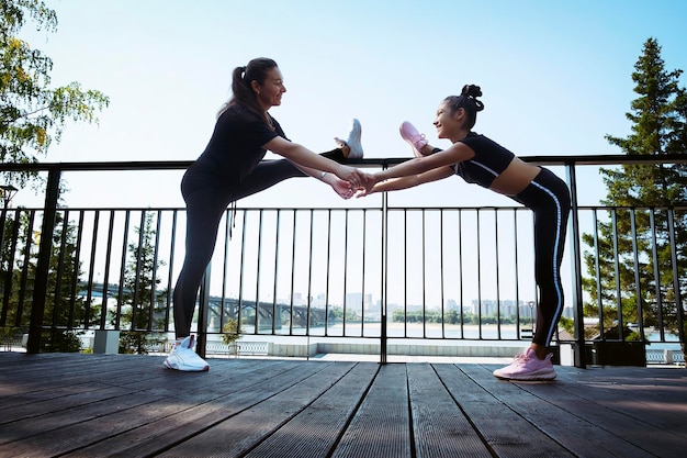 mamá e hija en ropa deportiva en un día soleado de verano en el terraplén del parque haciendo fitness