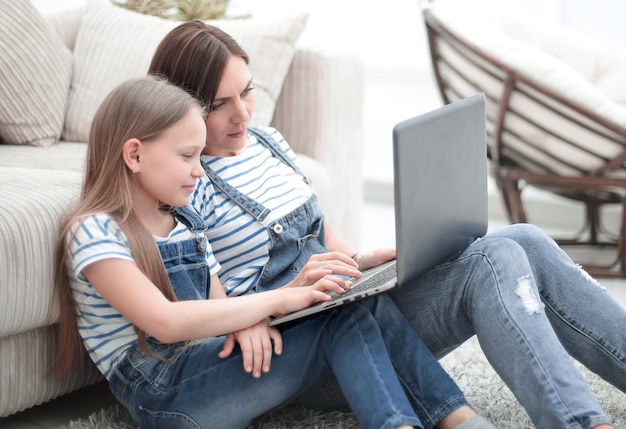 Mamá e hija sentadas en la alfombra en la sala de estar y usando una foto de computadora portátil con espacio para copiar
