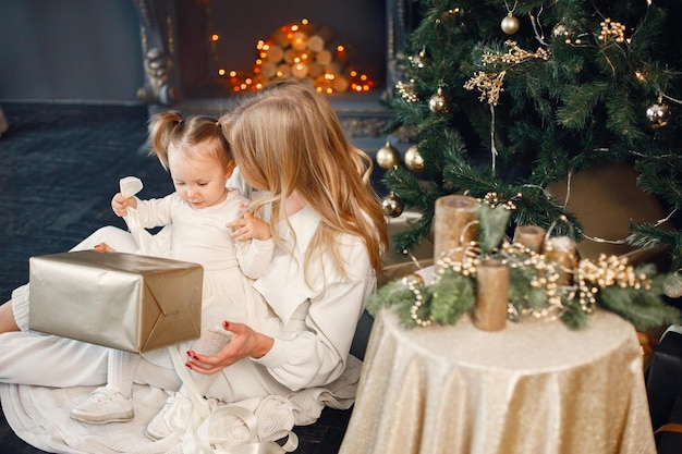 Mamá e hija sentadas cerca del árbol de Navidad y sosteniendo un regalo