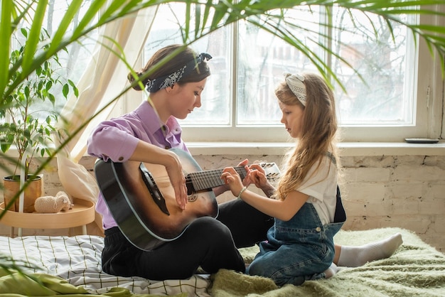 Mamá e hija en el sofá tocando la guitarra, una mujer y una niña componen canciones musicales juntas