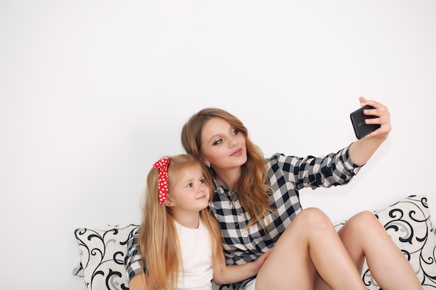 Mamá e hija tomando selfie mientras descansa en la cama en casa.