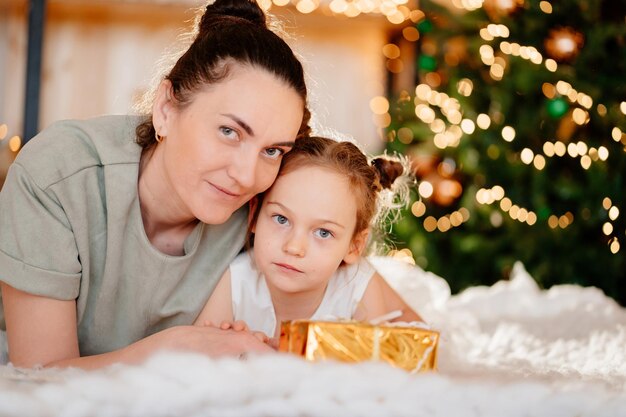 Mamá e hija en vestido blanco con regalo en papel de regalo dorado