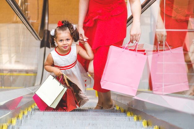 Mamá e hija en vestidos en el centro comercial con bolsas de colores.