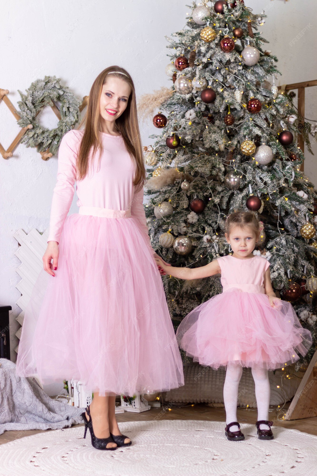 Mamá e hija con vestidos de tul rosa idénticos se cerca del árbol de navidad | Foto Premium