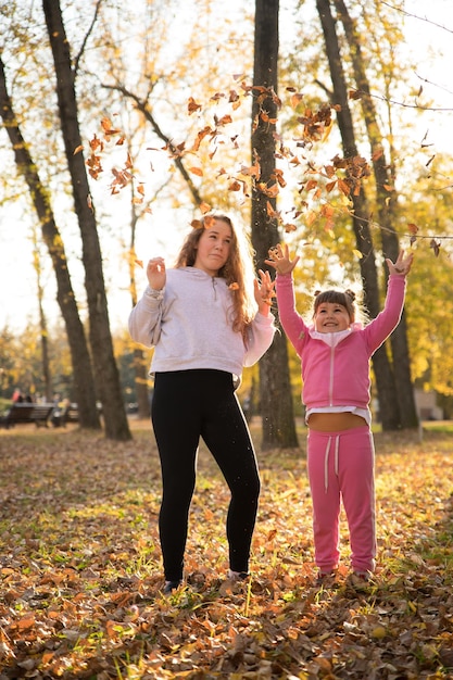 Mamá e hija vomitando hojas muertas en el parque de otoño