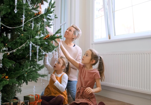 Foto mamá e hijas decoran un árbol de navidad sentados en el suelo de la sala de estar