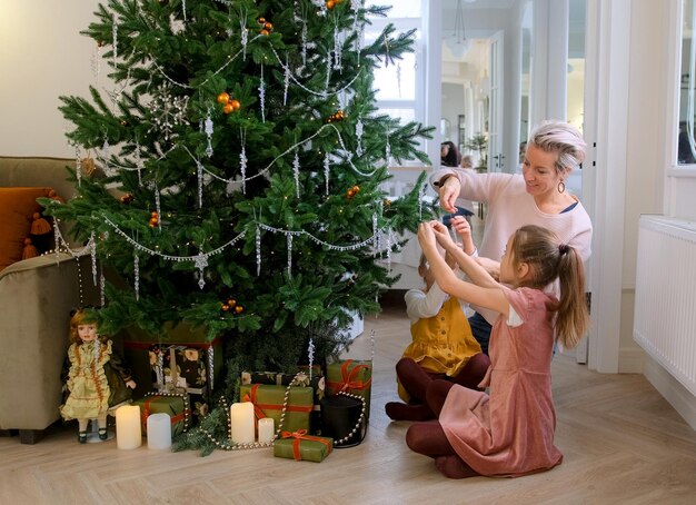 Foto mamá e hijas decoran un árbol de navidad sentados en el suelo de la sala de estar