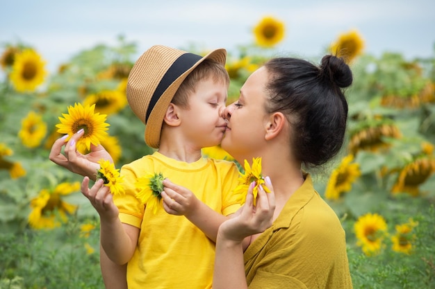 Mamá e hijo se abrazan, ríen y juegan en un campo de girasoles.