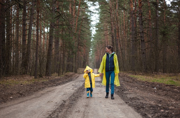 Mamá e hijo caminando por el camino forestal después de la lluvia en impermeables juntos