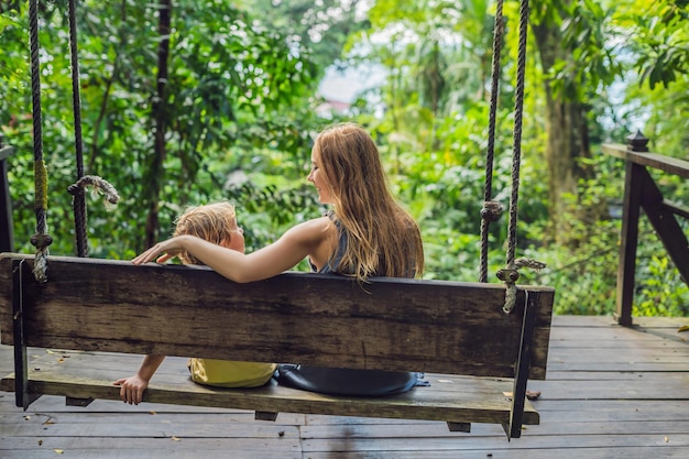 Foto mamá e hijo en un columpio en un jardín tropical