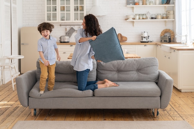 Mamá e hijo se divierten en la sala de estar peleando con almohadas juntos tiempo de recreación y ocio familiar